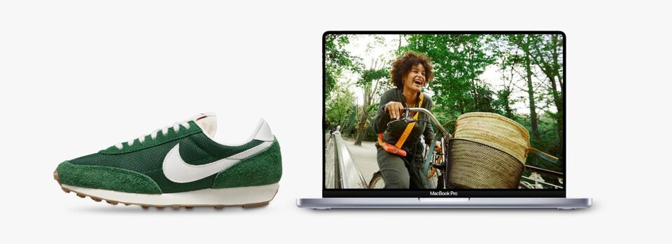 An Apple MacBook Air displays a picture of a person smiling while riding a bike outdoors. To the left of the laptop is a green WMNS Nike Daybreak vintage 'Fir Coconut Milk' sneaker.