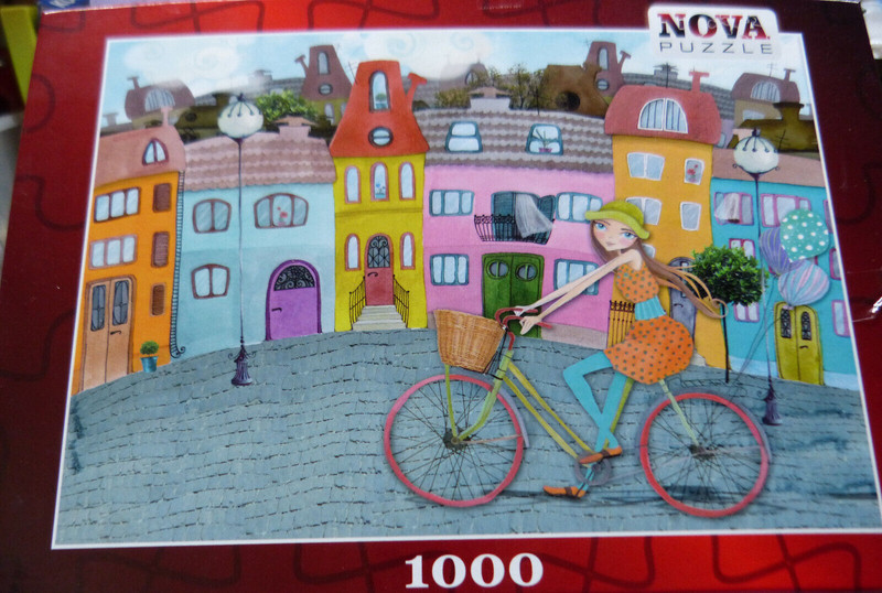 25187. Puzzle Radfahrerin Vor  HÃ¤Userfront   1000 Teile  Nova