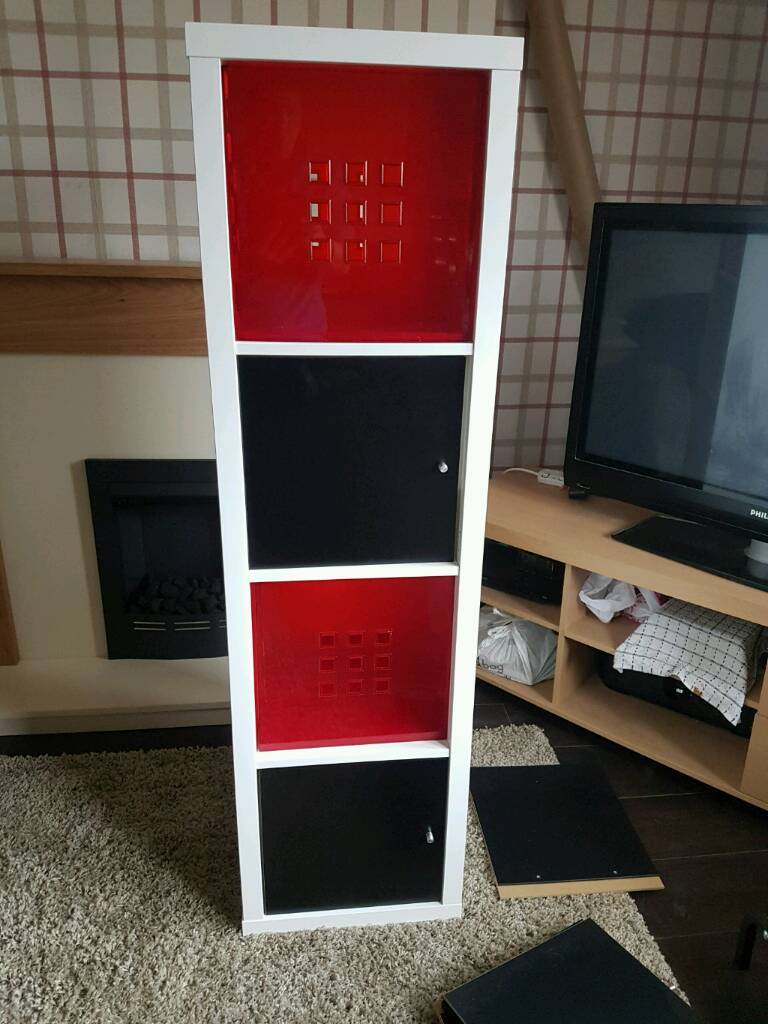 White Ikea kallax unit. 2 red plastic storage boxes &2 black doors in