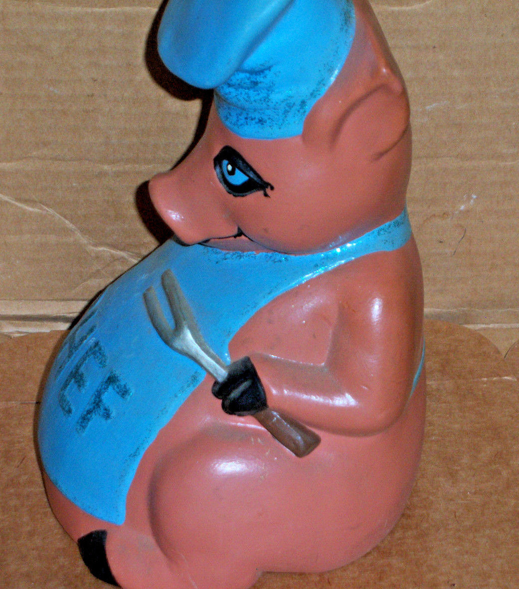 Pig holding a silver fork and wearing a blue apron marked CHEF