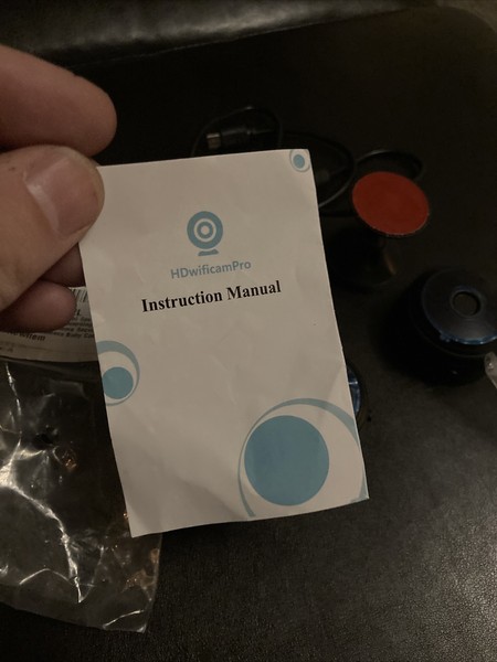 Hand holding HDWifiCamPro instruction manual with blurry background.