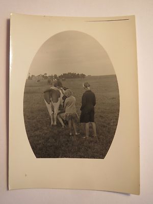 Mädchen im Kleid auf Weide - Frau melkt eine Kuh / Foto