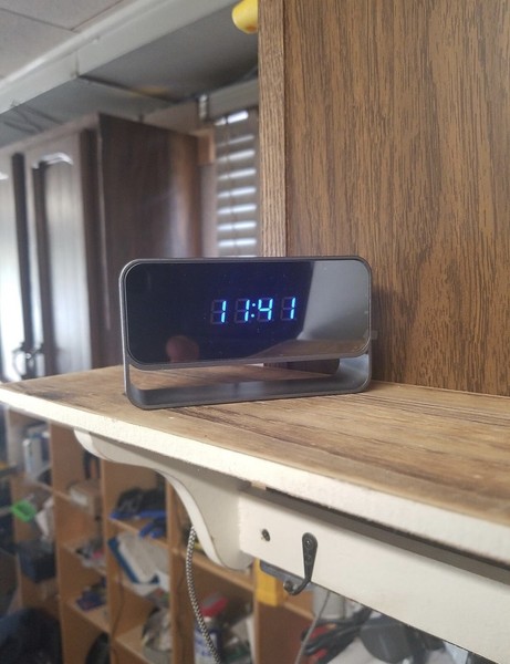 Digital clock displaying time on wooden shelf.