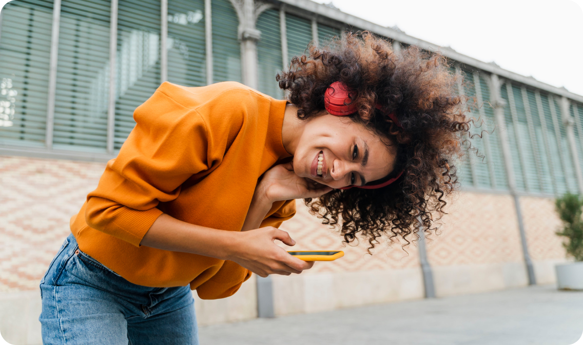 A person wearing red headphones and holding a yellow phone linking to Refurbished electronics page