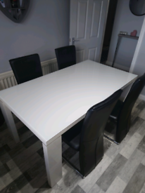 Large white glass dining room table and four black chairs