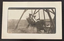 1912 REAL PHOTO POSTCARD 2 MEN SITTING ON A WOODEN SWING IN OUTDOOR FIELD USED