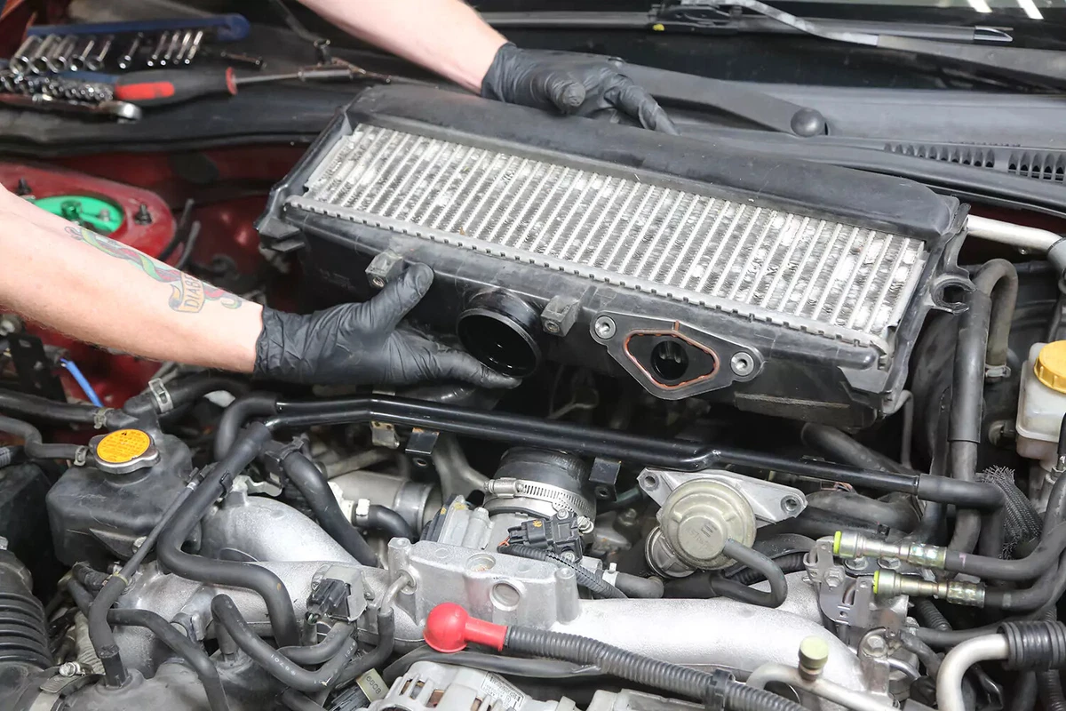 A mechanic wearing black gloves removes engine components to gain access to the PCV valve.