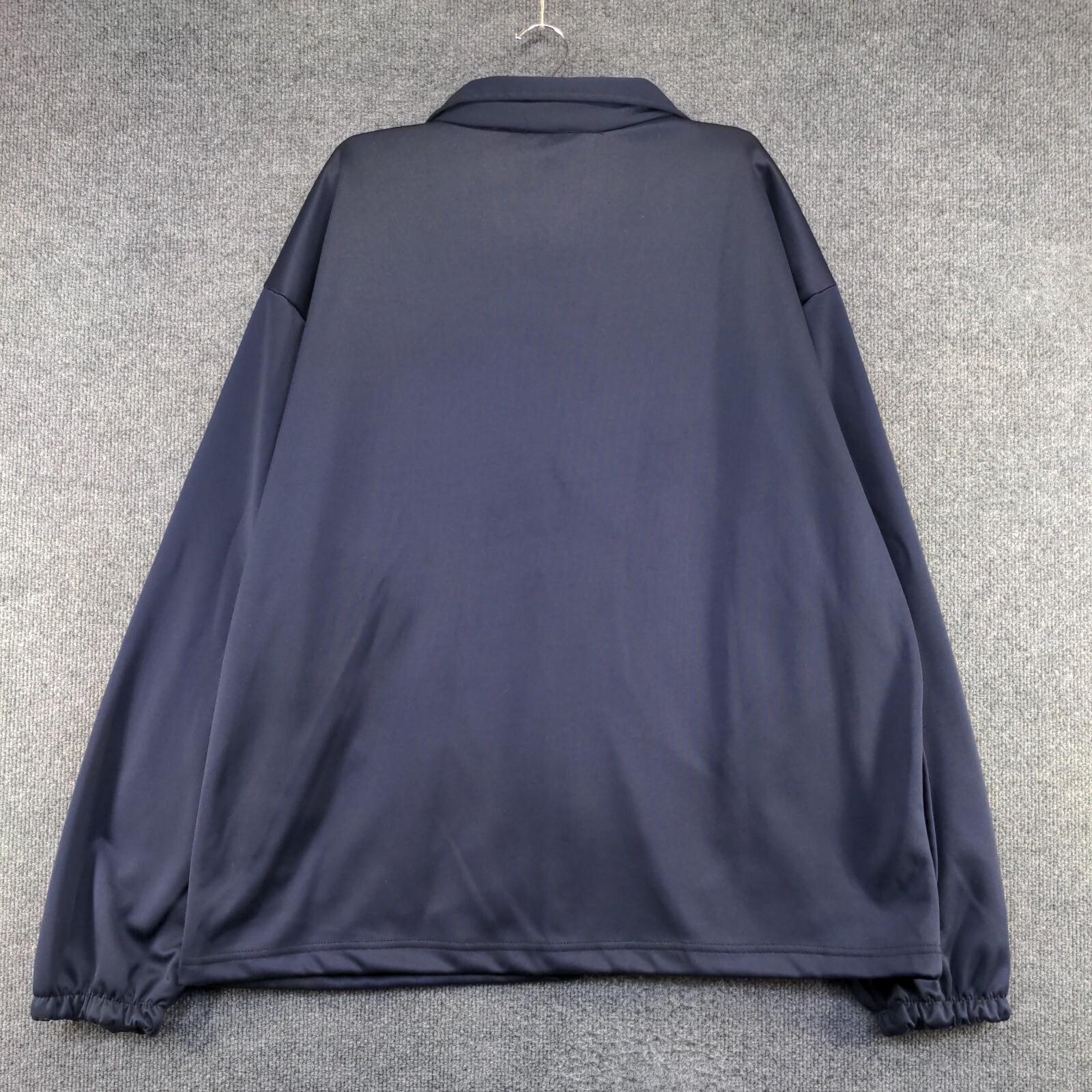 Dark blue men's full zip jacket with elastic cuffs, hanging on a gray hanger against a light gray wall.