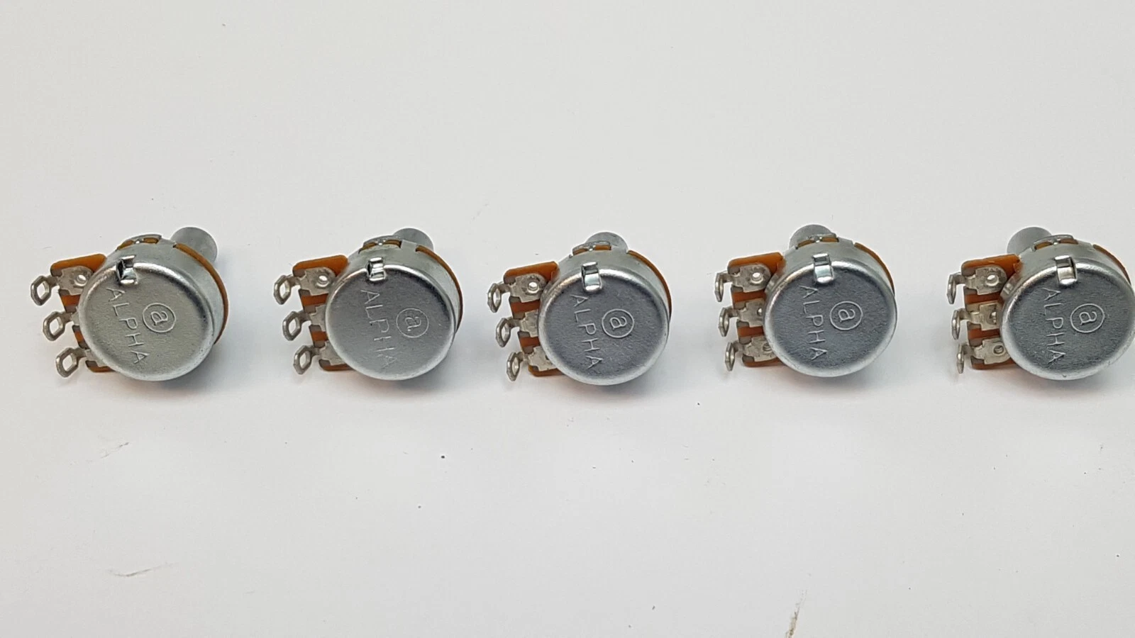 Back of five Alpha potentiometers showing the Alpha logo on the metal case