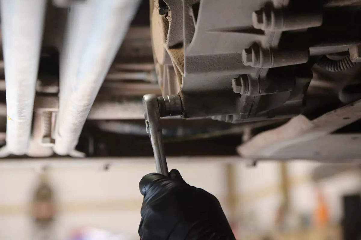A mechanic wearing a black glove uses a torque wrench to tighten the drain plug on the transfer case.