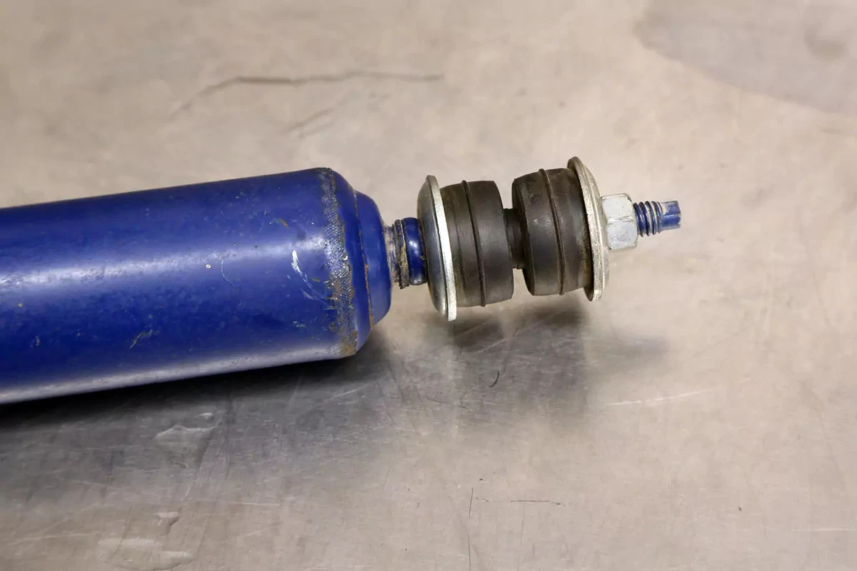 A blue shock absorber with a bayonet shock mount on a steel work surface.