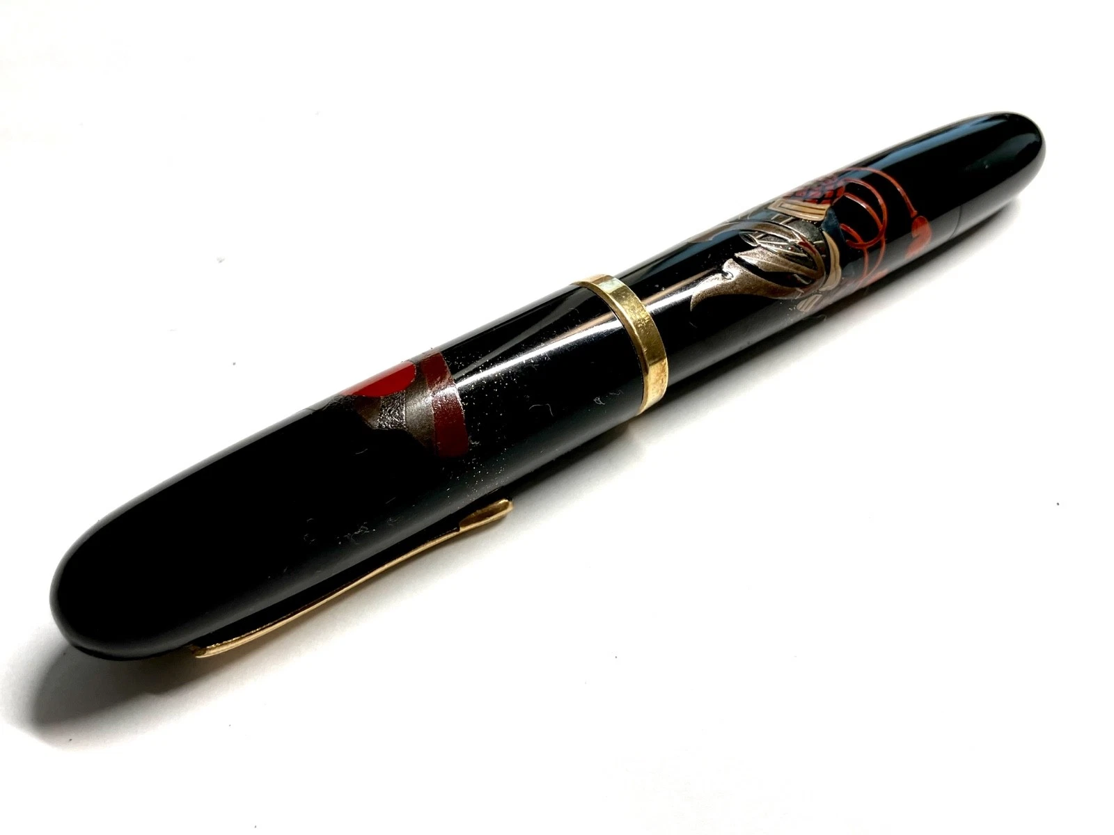 Black vintage fountain pen with gold accents, red and brown ink blotels, and “HARUYAMA made urushi makie Kabuto” text on body.