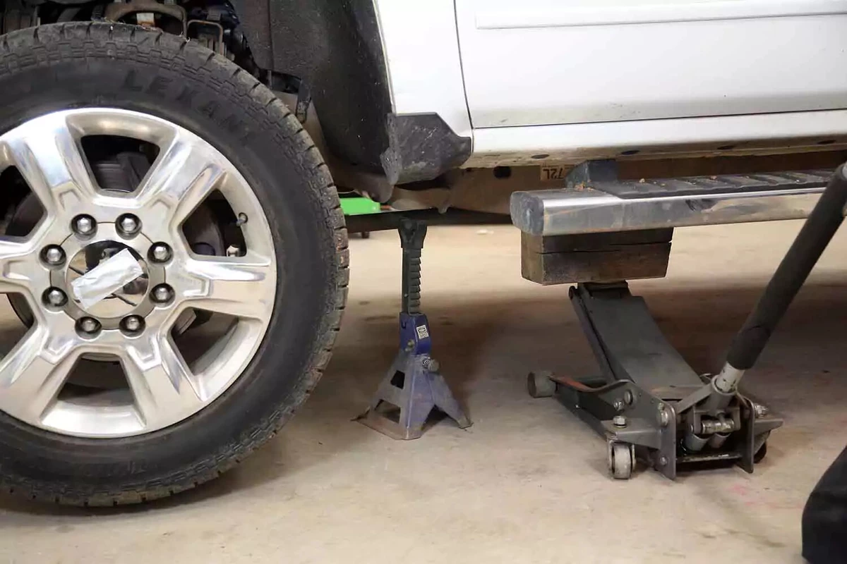 A pickup truck lifted with a floor jack, jack stand, and wood blocks.