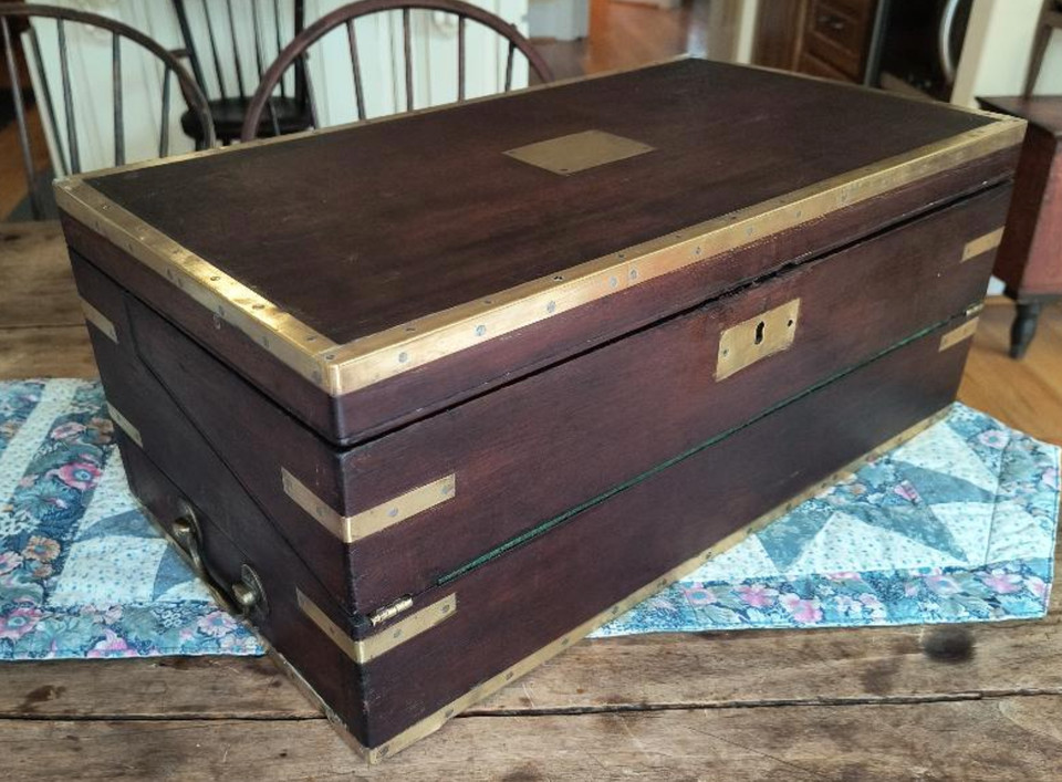 A 19th-century mahogany campaign lap desk with brass binding and a dovetailed drawer — a genuine piece of portable history that doubles as the most distinguished desk accessory imaginable.