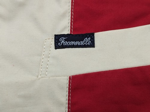 White fabric label with blue “Faconnable” text, red and blue diagonal stripes, and stitched seam detail.