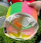 White snapback hat with multicolor panels in yellow, pink, green, and blue, featuring mesh fabric and tan logo patch.