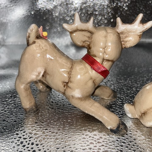 Pair of vintage Christmas reindeer figurines, one lying on silver ground with red collar, one standing with white antlers.