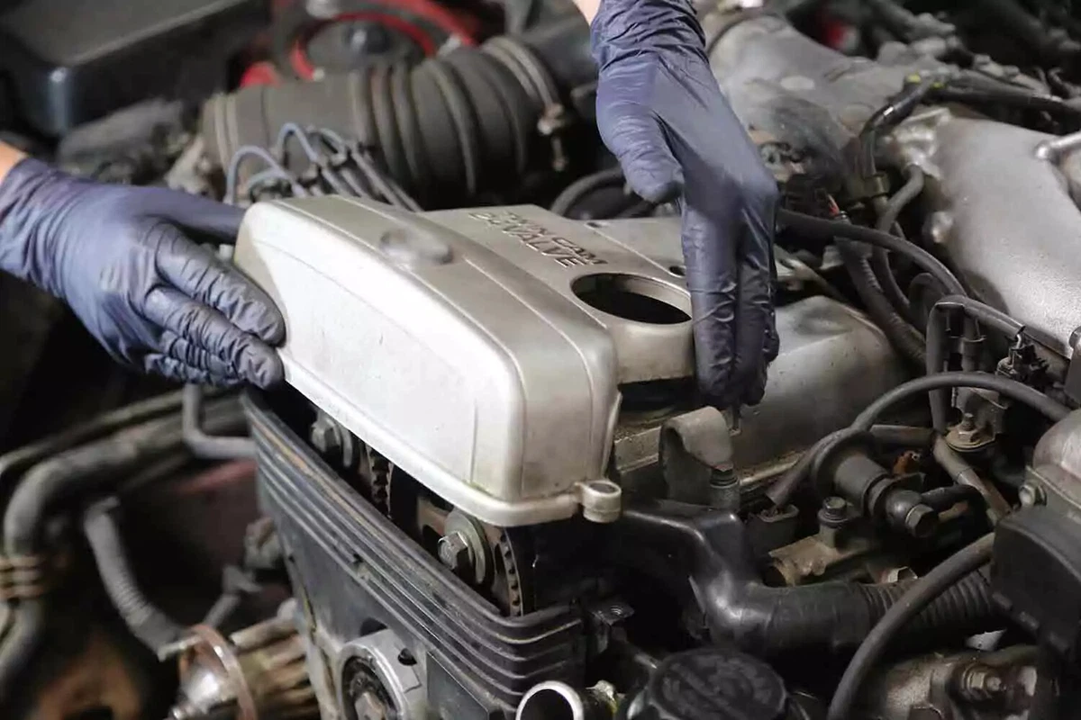 A mechanic wearing blue nitrile gloves removes an engine’s upper timing belt cover, exposing the timing belt.