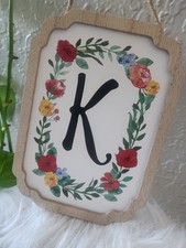Hanging Wooden sign featuring a floral wreath desing surrounding the letter k
