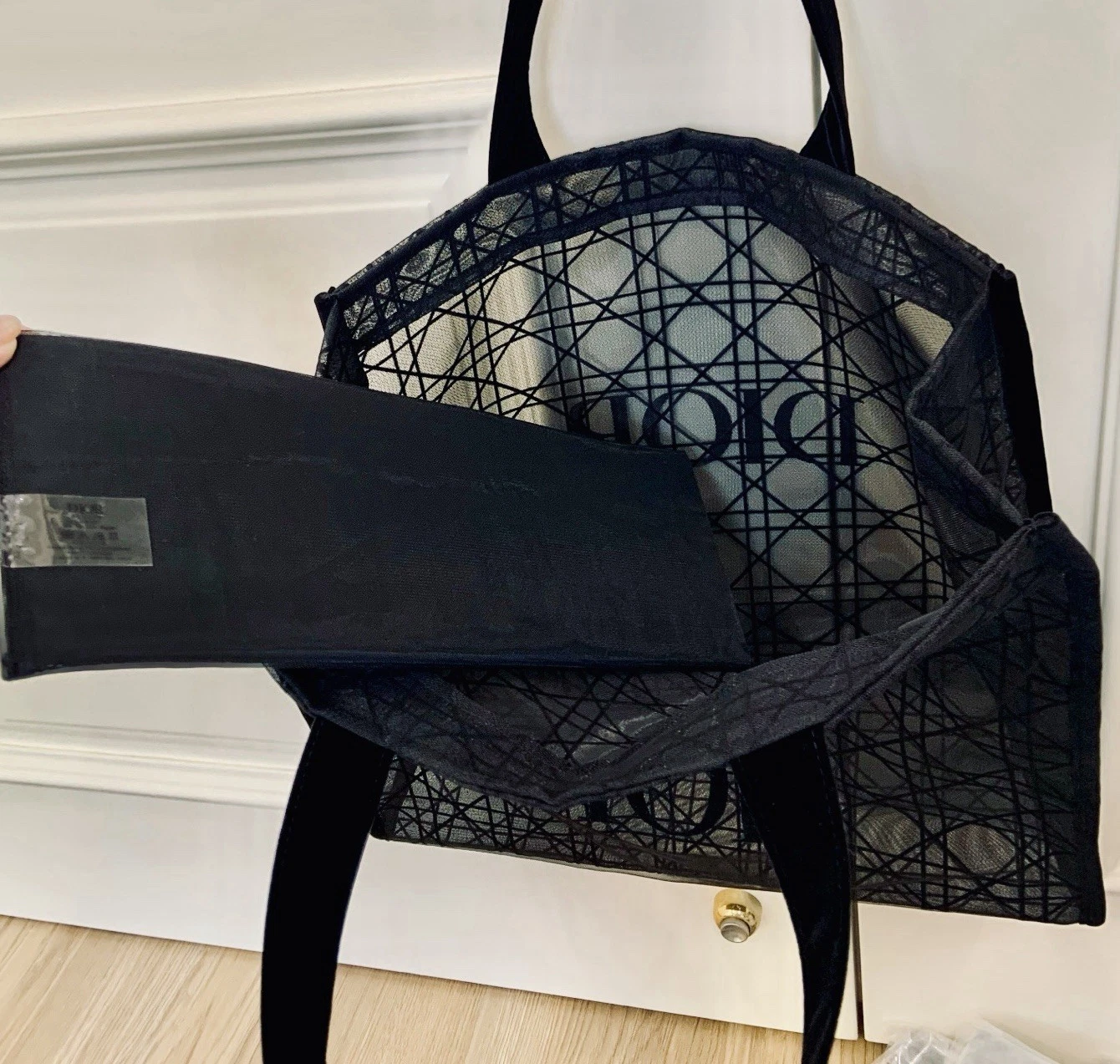 Black lace mesh tote with geometric pattern, tan leather handles, and folded black strap with silver hardware.