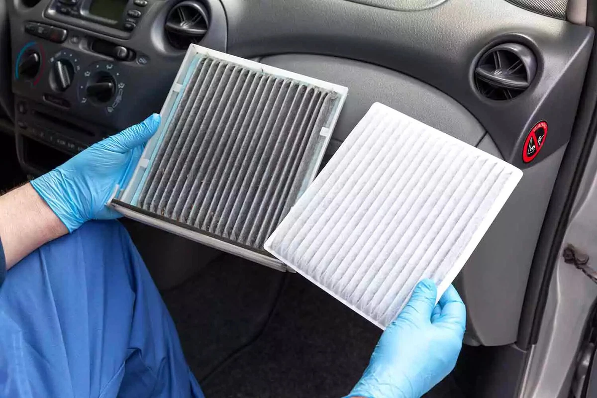 A mechanic wearing blue nitrile gloves compares a dirty cabin air filter with a fresh new filter.