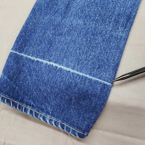 Close-up of worn blue denim high-rise straight leg with white stitching and a yellowed metal measuring tape across the waistband.
