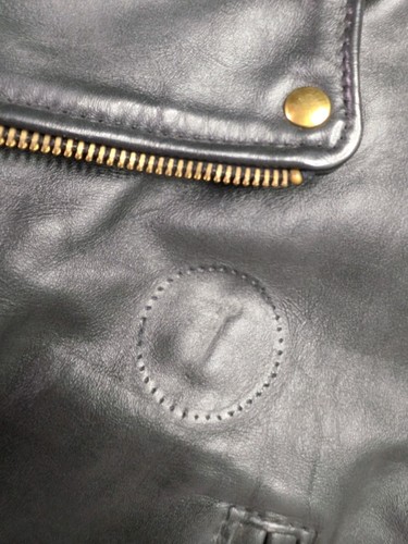 Black leather Langlitz motorcycle jacket with gold zipper, button closure, and circular gold emblem on left chest.