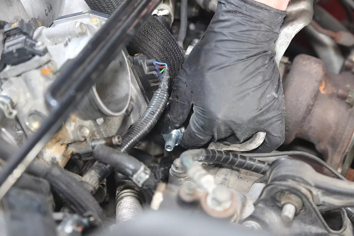 A mechanic wearing a black glove installs a new PCV valve into a vehicle's engine.