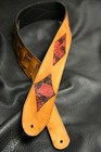 Brown leather guitar strap with red and black diamond inlay pattern, two fastening holes, and visible “Made in USA” text.