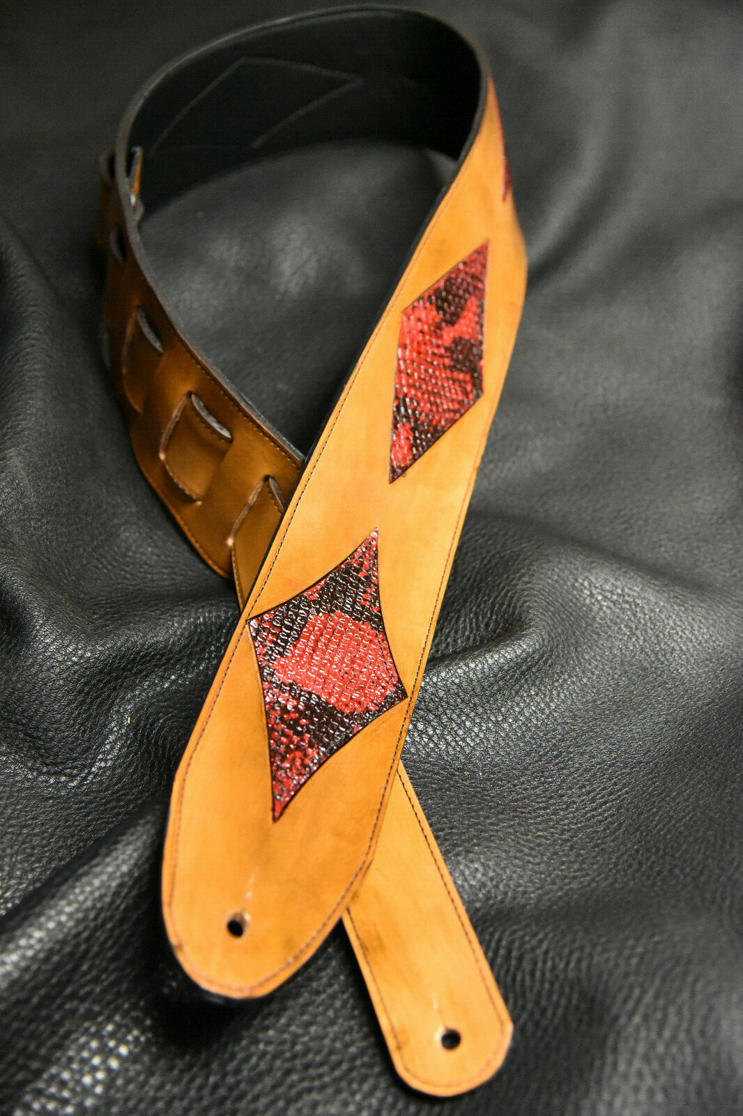 Brown leather guitar strap with red and black diamond inlay pattern, two fastening holes, and visible “Made in USA” text.