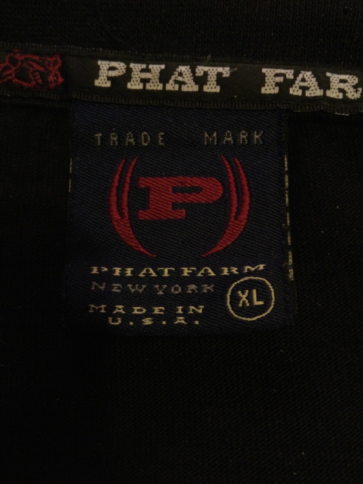 White fabric tag on black shirt with red “PHAT FARM” text, red and black logo, and “Made in U.S.A.” label.