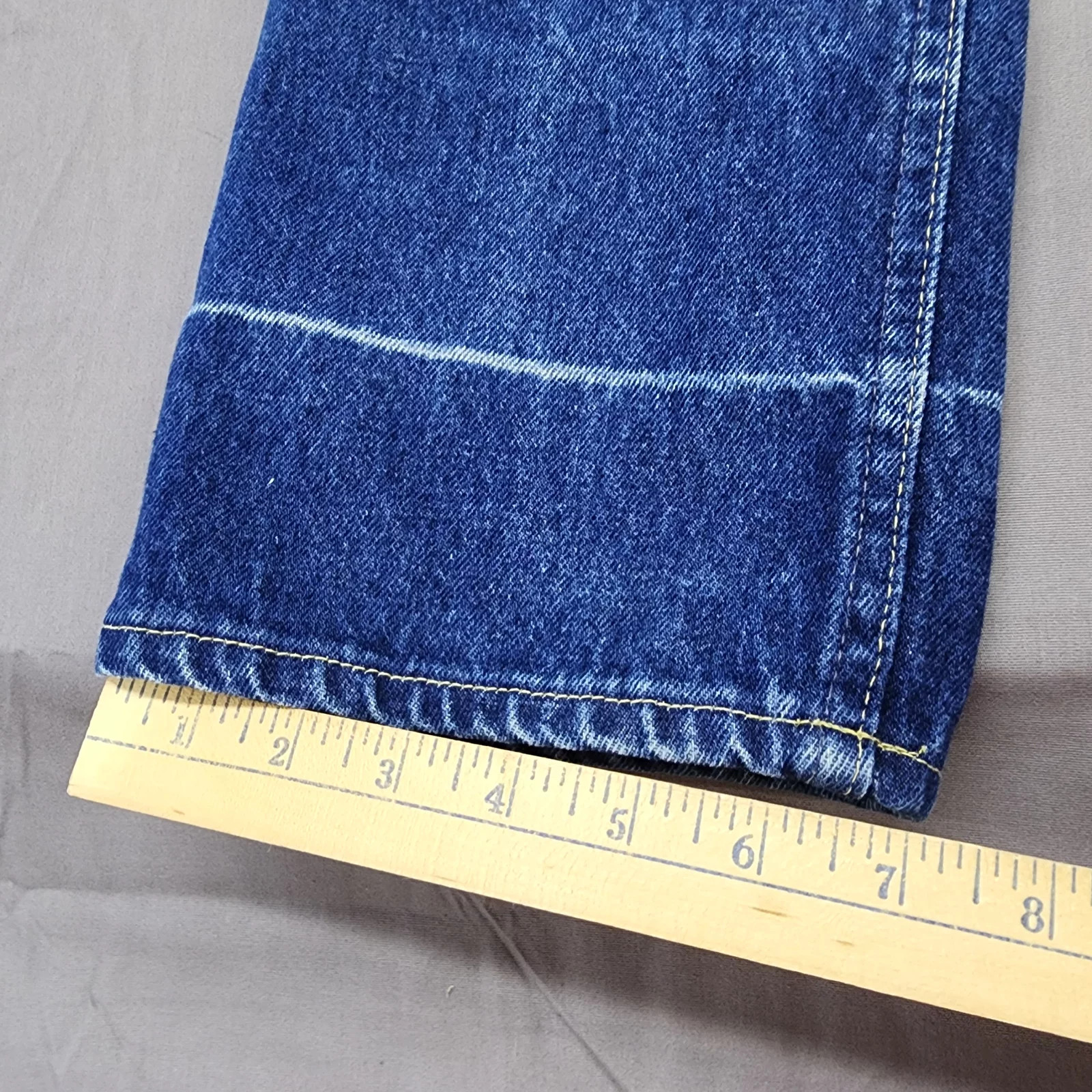 Blue denim high-rise straight leg with white contrast stitching, yellow measuring tape across the bottom.