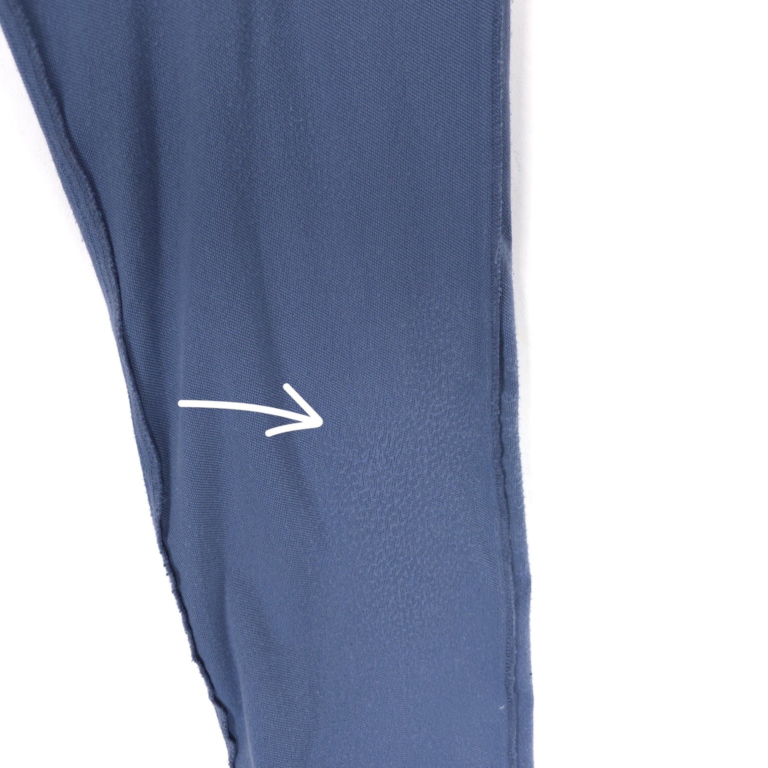 Close-up of a seam on a blue dress pant leg with white zigzag stitching and a small white arrow graphic.