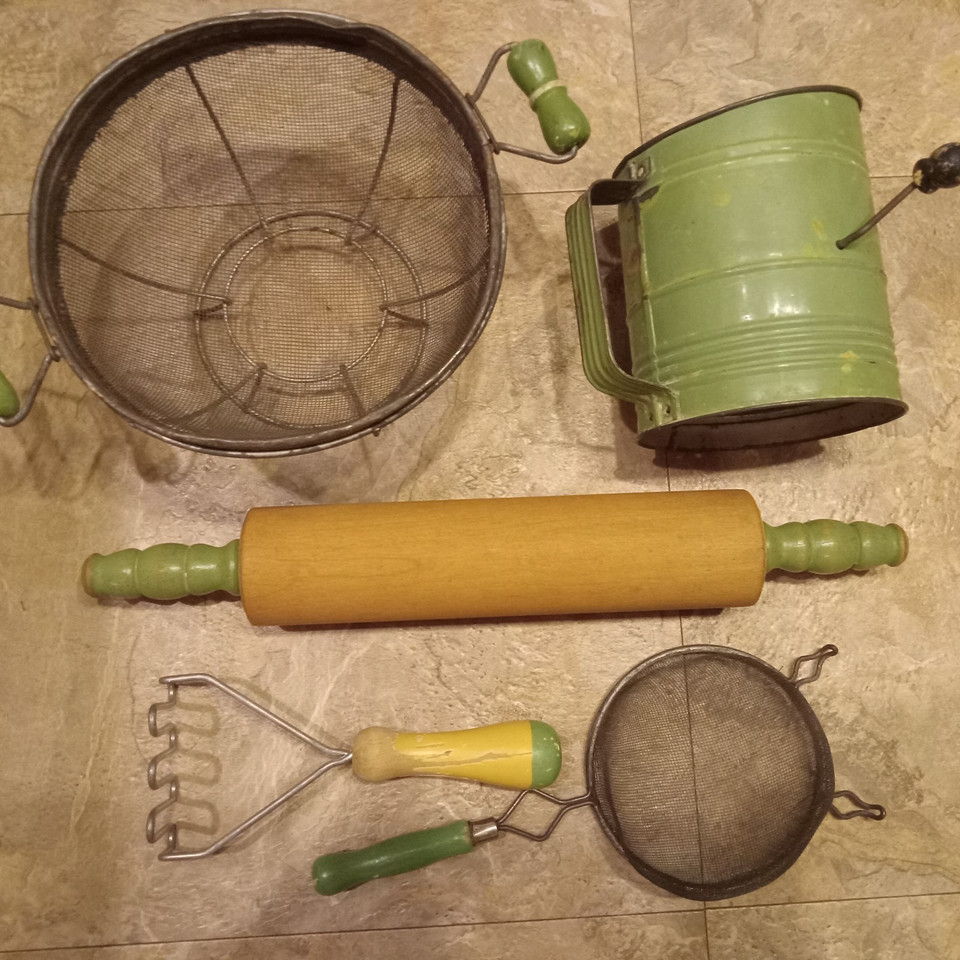 A matching cream-and-green vintage kitchen set — rolling pin, masher, sifter, and strainers — that looks like a styled prop from a mid-century farmhouse shoot.