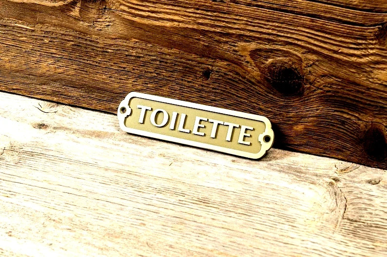 Solid brass 'TOILETTE' door plaque with nautical detailing — the kind of understated, material-quality piece that elevates any bathroom instantly.