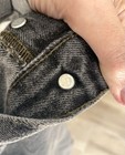 Close-up of worn black Levi’s 501 XX jeans with silver rivets and button fly closure, showing metal rivets and yellow stitching.