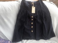 “A navy linen button-front A-line skirt with a high waist and soft pleating