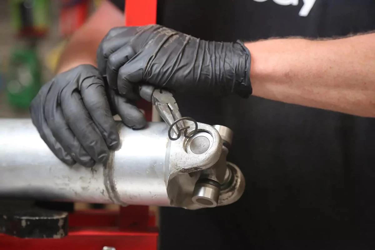 A mechanic wearing black gloves installs a clip into the opposing yoke ear.