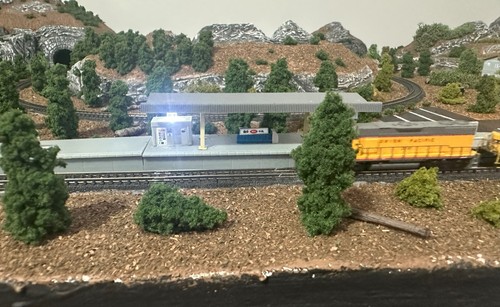 Z scale model train layout with yellow Pacific locomotive, station platform, trees, rocks, and curved track in mountainous terrain.