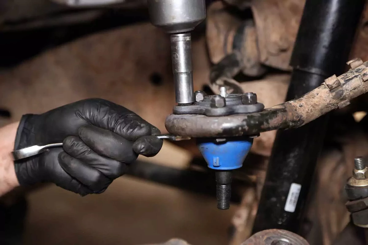 A mechanic uses an impact wrench and a box wrench to bolt the new ball joint to the upper arm.