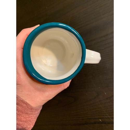 Teal green ceramic coffee mug with white ribbed beehiive, held in a hand against a dark background.