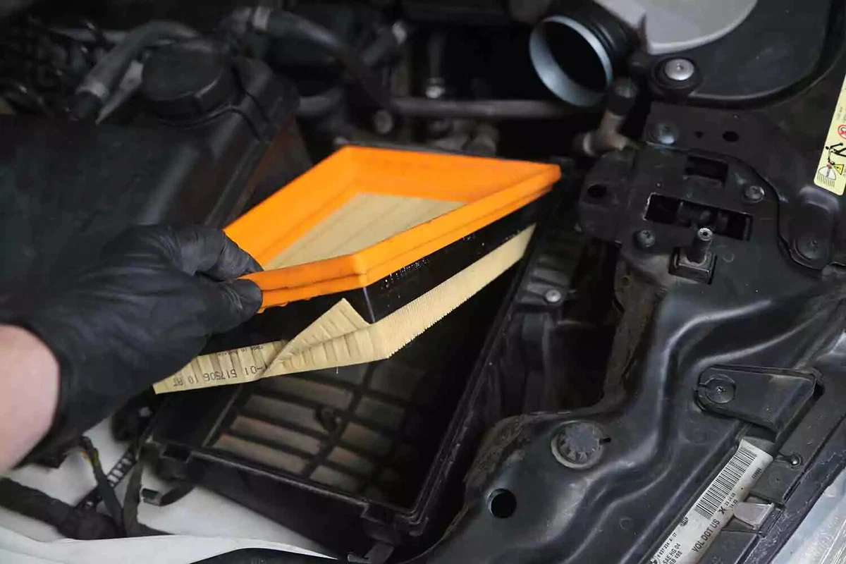 A mechanic wearing a black nitrile glove installs a new air filter.