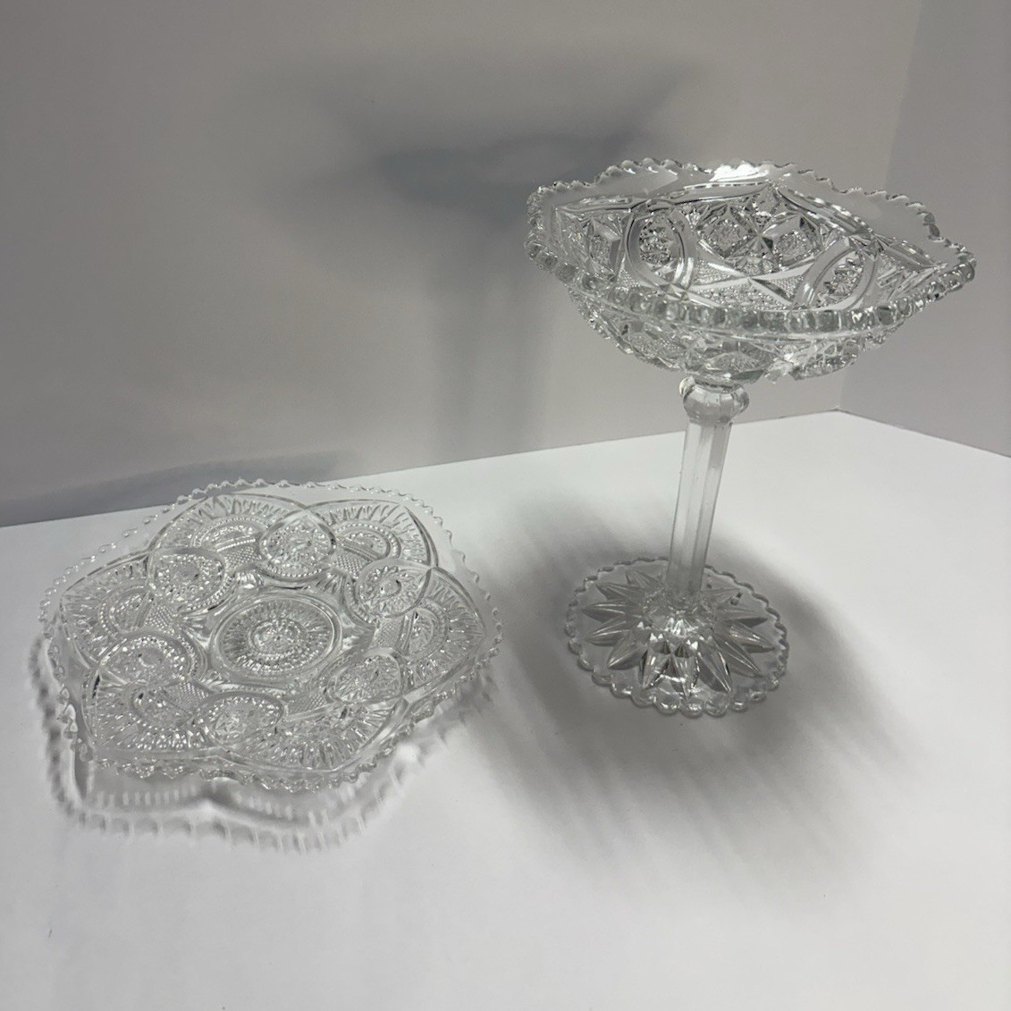Clear pressed glass pedestal compote dish with a matching flat serving plate.