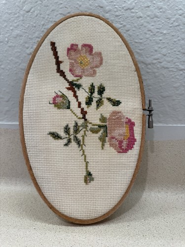 cross-stitch embroidery of pink wild roses in an oval wooden hoop.