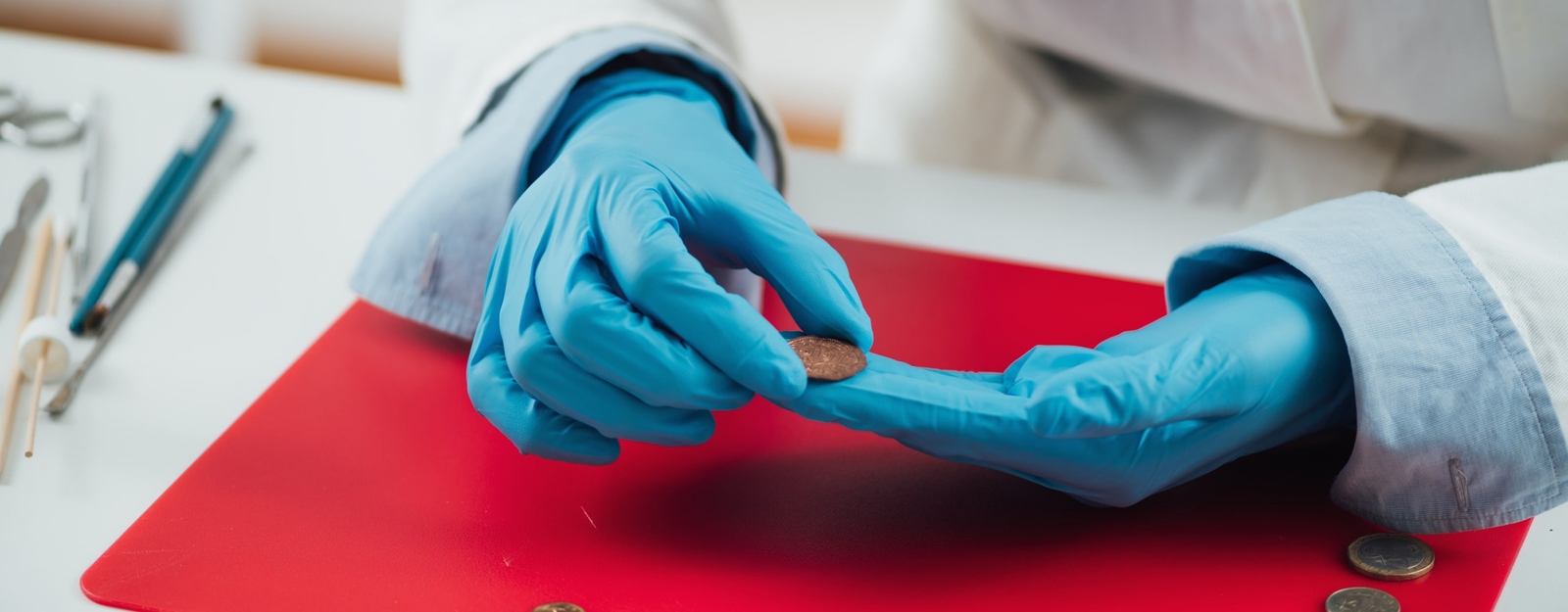 Eine Person mit blauem Gummihandschuhen begutachtet eine Münze