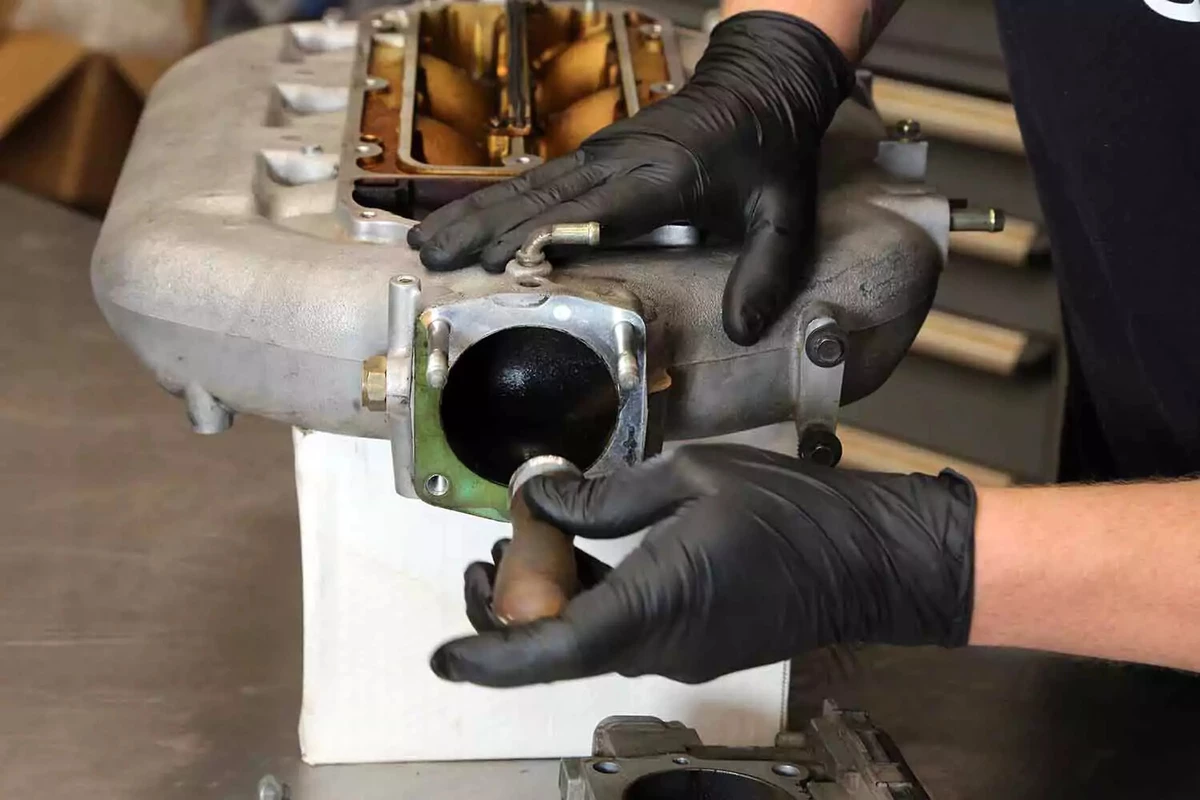 A mechanic uses a gasket scraper to remove residue from the old gasket that remains on the intake manifold’s sealing surface.