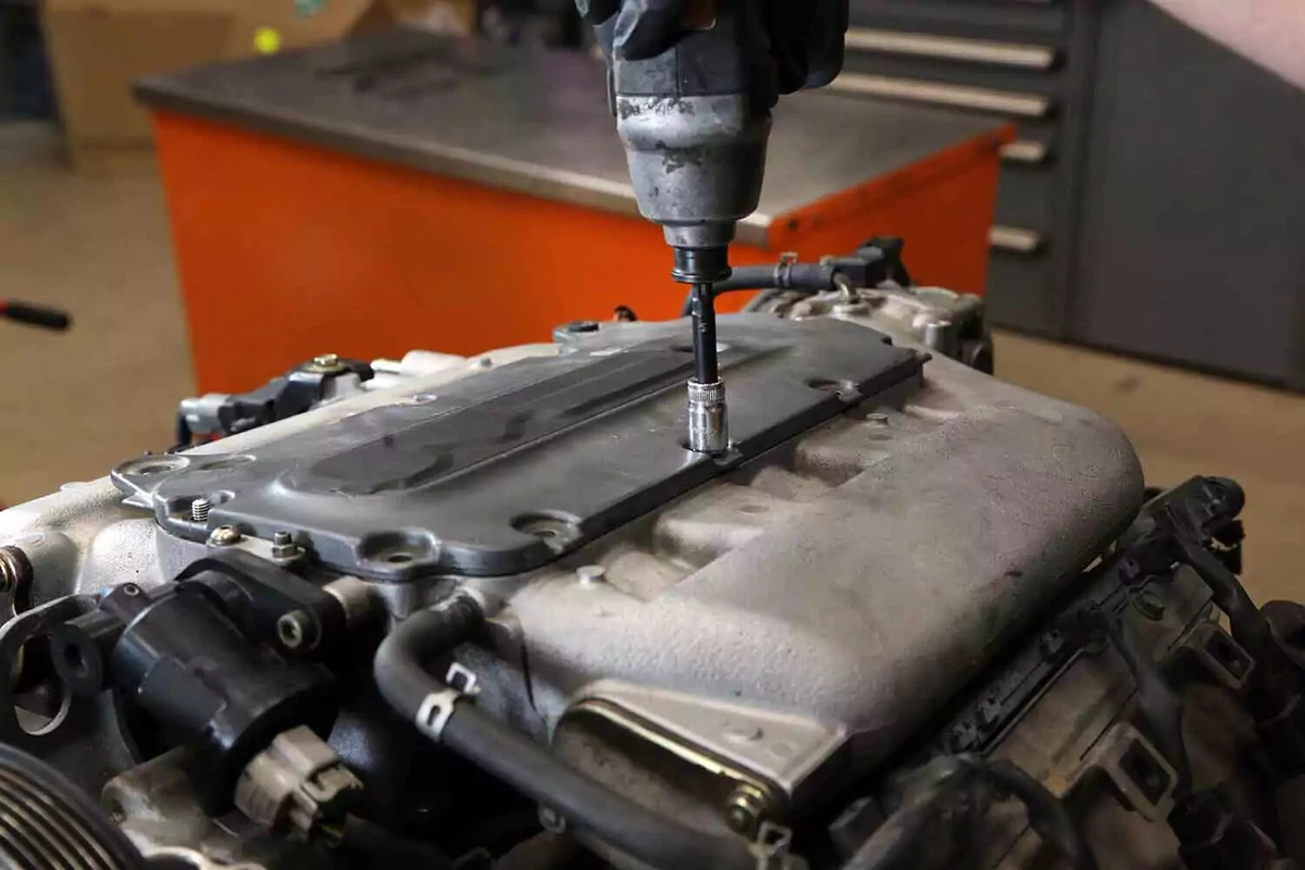 A mechanic removes a bolt from an intake cover using an impact driver.