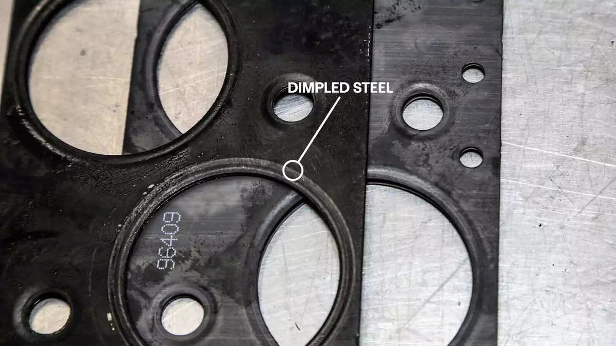 An old intake gasket displayed on top of a new gasket on a metal work surface.