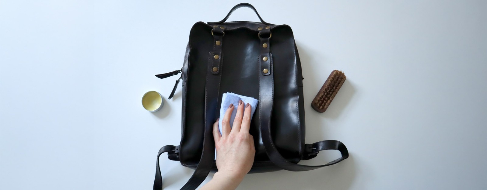 Eine Hand, die mit einem Tuch die Rückseite eines Lederrucksacks pflegt.