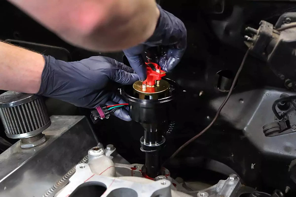 A mechanic lowers the new distributor into the engine, taking care to engage the oil pump drive shaft.